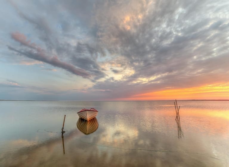 Hvid robåd med rød kant på stille vand ved solnedgang