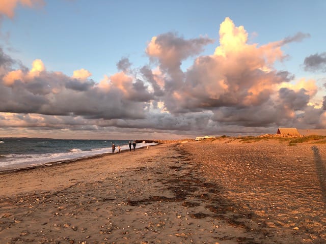 Stenstrand ved solnedgang med skyer og hav